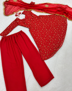 A red three-piece traditional outfit laid flat on a white textured background, including a long-sleeve top with a small gold floral print, solid red pants, and a matching sheer red dupatta with gold border detailing.