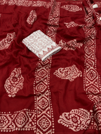 A close-up of a deep red fabric with beige block-printed floral and geometric patterns, featuring a folded matching patterned fabric piece placed on top.