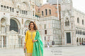 Woman in a yellow and green traditional outfit standing in front of a historic building.