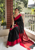 Woman in a black and red saree sitting on a balcony.