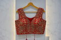 Red embroidered blouse on a hanger with 'Red' label, floral decorations in the background