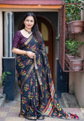Woman wearing a dark blue saree with floral patterns standing in front of a door.