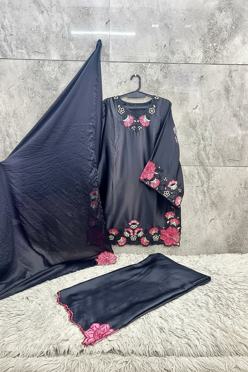 Black embroidered dress with pink flowers on a hanger against a gray tiled wall.