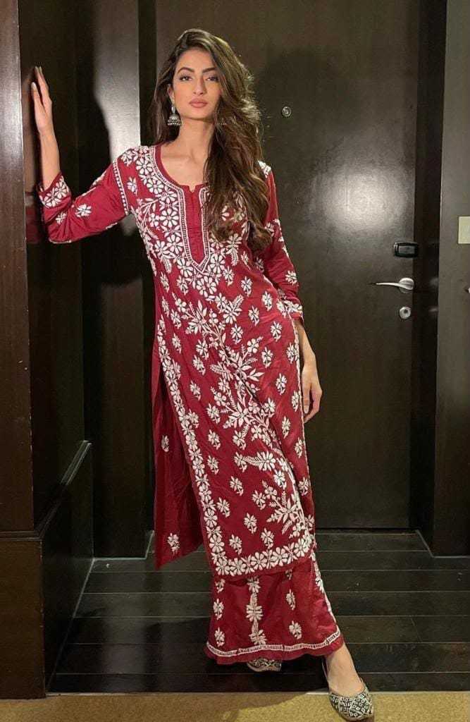 Woman wearing a red embroidered traditional outfit standing in a doorway.