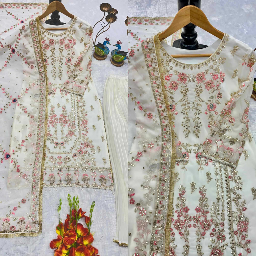 A traditional white embroidered women's outfit displayed on hangers, featuring a floral pink and gold embroidered kurta, matching white pleated pants, and a sheer embroidered dupatta, arranged on a light patterned fabric background with decorative peacocks and flowers.