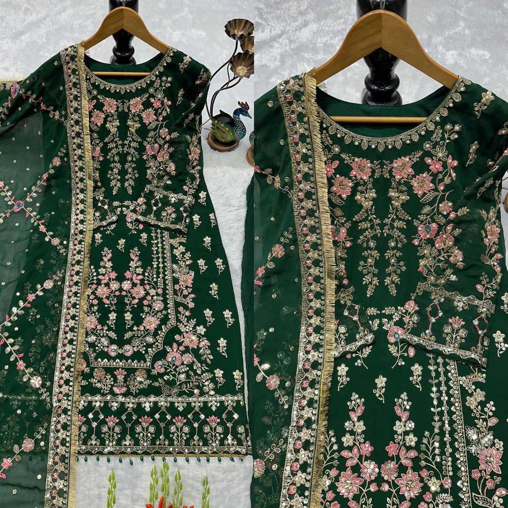 Two dark green embroidered traditional outfits hanging on wooden hangers against a light textured backdrop. The garments feature intricate floral embroidery in pink, white, and gold, with a matching sheer green dupatta draped over one of the hangers.