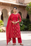 Woman wearing a red traditional outfit with floral patterns in an outdoor setting.