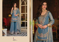 Woman in a blue embroidered traditional outfit standing in a decorated room.