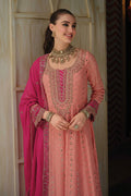 A woman modeling a peach-pink embroidered traditional outfit with a bright pink dupatta, standing in front of a light wooden door. The image features the brand logo 'Laam' in the top right corner.