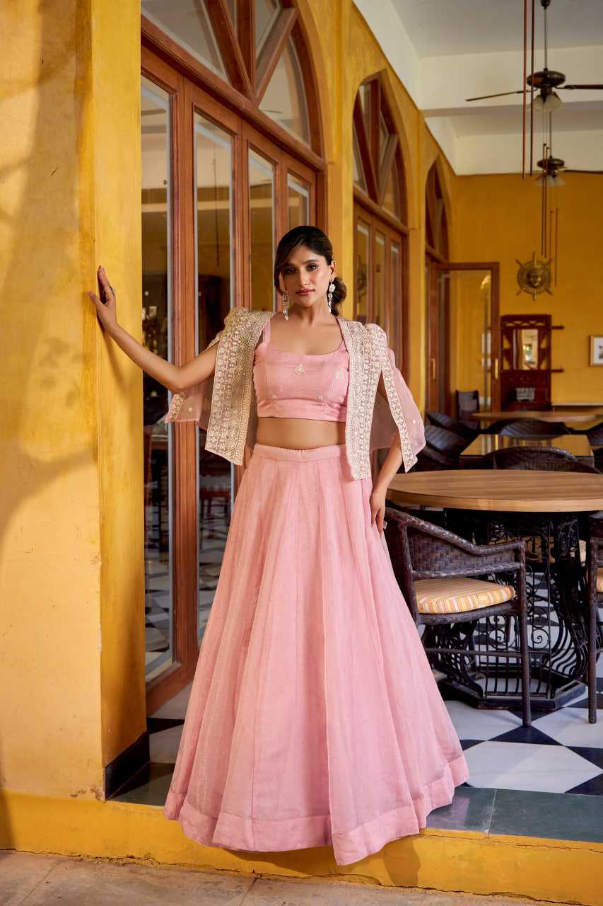 Woman in a pink traditional outfit standing in a restaurant with yellow walls and wooden furniture.