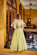 Woman in a light green traditional outfit standing in a restaurant with yellow walls and black and white checkered floor.