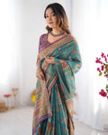 Woman wearing a teal saree with a colorful border in a minimal indoor setting