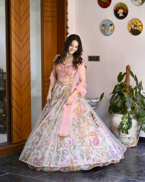Woman in a floral and pink traditional outfit standing indoors with decorative plates on the wall.