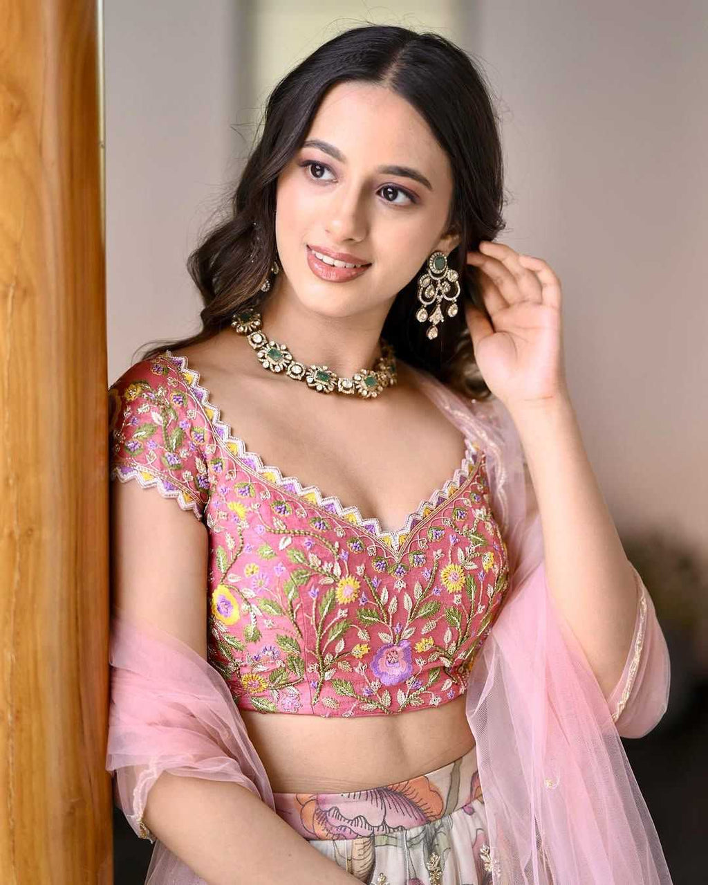 Woman wearing a pink floral blouse with a matching dupatta, posing indoors.