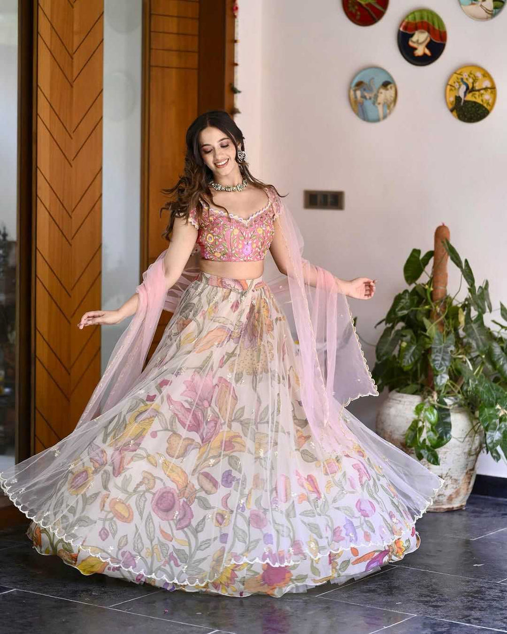 Woman in a floral lehenga dancing indoors with decorative plates on the wall.