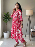Woman wearing a pink floral dress standing in a room with a plant and lamp.