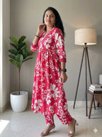 Woman wearing a pink floral dress standing in a room with a plant and lamp.