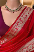 A red silk saree with intricate gold Banarasi floral zari embroidery, styled with a deep purple blouse and a matching red and green beaded necklace. The word 'Red' is printed on the left side.