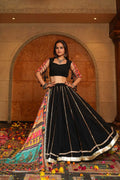 Woman in a traditional black and colorful outfit standing in a decorated indoor setting.