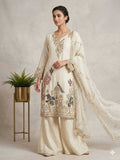 Woman wearing a cream embroidered traditional outfit with a plant in the background