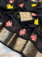 Black silk saree fabric with pink and yellow floral embroidery and a wide gold zari border, shown folded with a matching embroidered cuff.