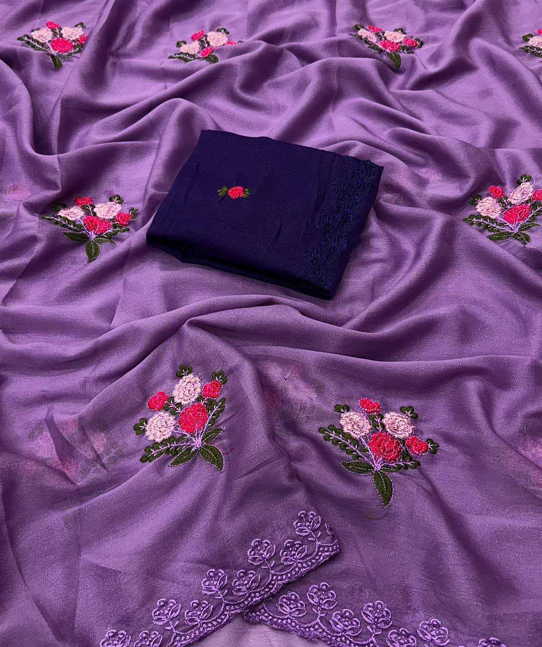 Purple embroidered fabric with floral motifs and a folded dark navy cloth piece placed on top, photographed as a styled product shot on a matching fabric background.