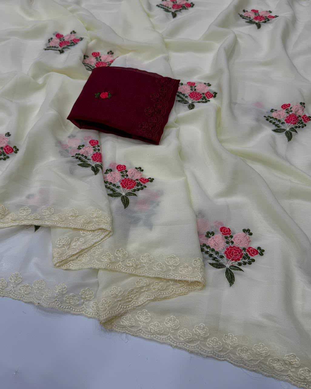 An off-white or cream-colored embroidered fabric, likely a dupatta or scarf, draped to show its floral embroidery and lace borders, with a folded dark red fabric piece placed on top.