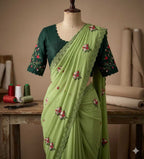 A light green saree with floral embroidery and a dark green embroidered blouse displayed on a dress form in a sewing studio setting.