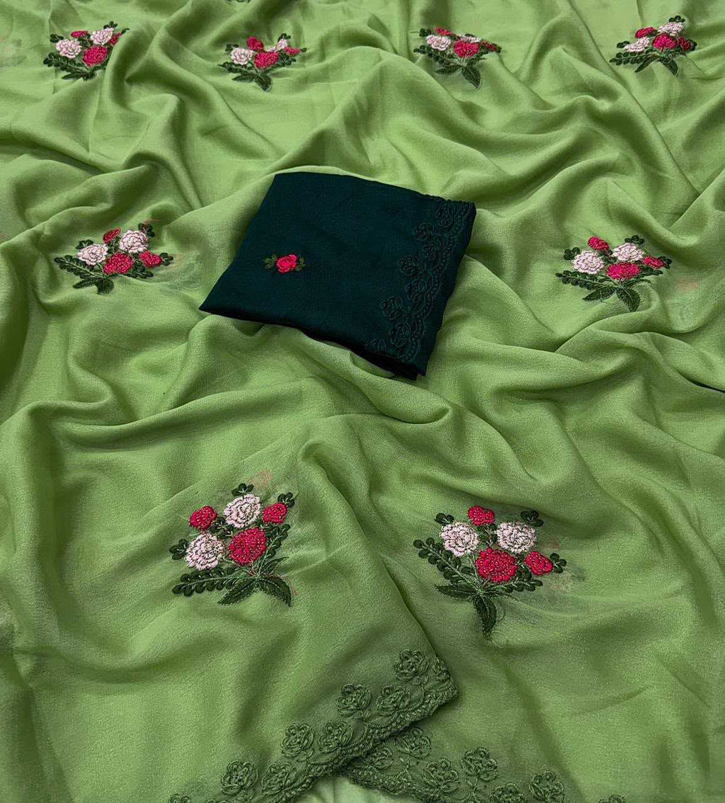 Green embroidered fabric with scattered floral motifs in pink, red, and white, plus a folded dark green fabric piece with lace trim placed on top.