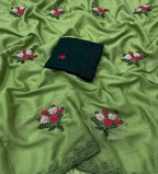 Green embroidered fabric with scattered floral motifs in pink, red, and white, plus a folded dark green fabric piece with lace trim placed on top.