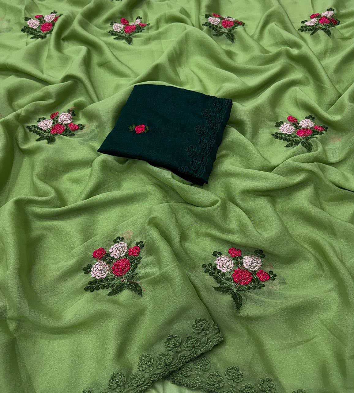 Green embroidered fabric with scattered floral motifs in pink, red, and white, plus a folded dark green fabric piece with lace trim placed on top.