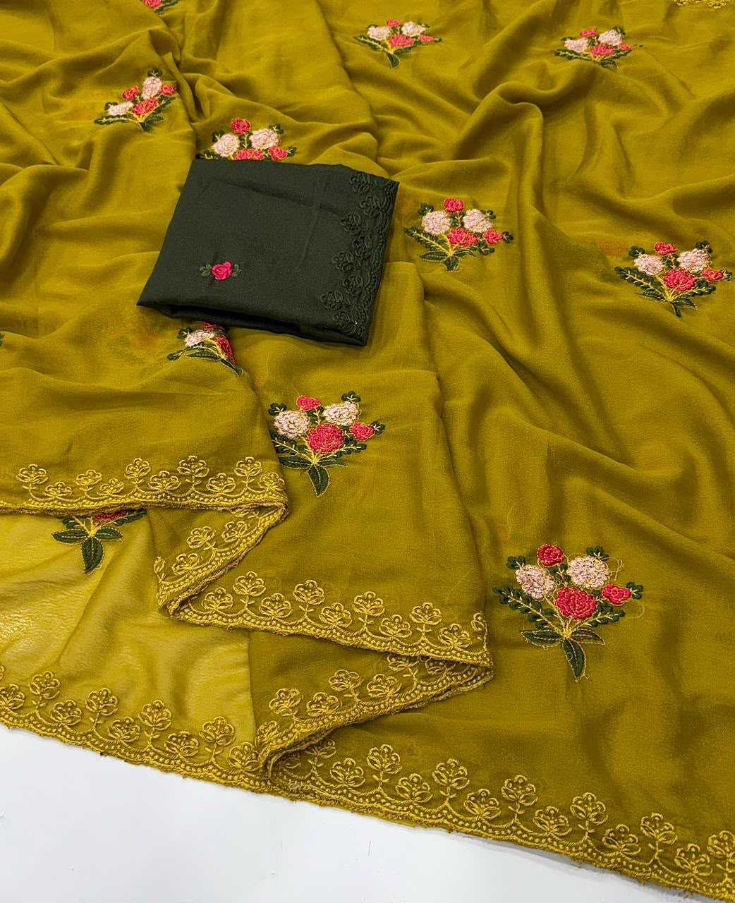 A mustard yellow fabric, likely a salwar suit material or dupatta, featuring embroidered floral motifs in pink, red, and green, with a gold embroidered border. A folded black fabric piece with matching embroidery is placed on top.
