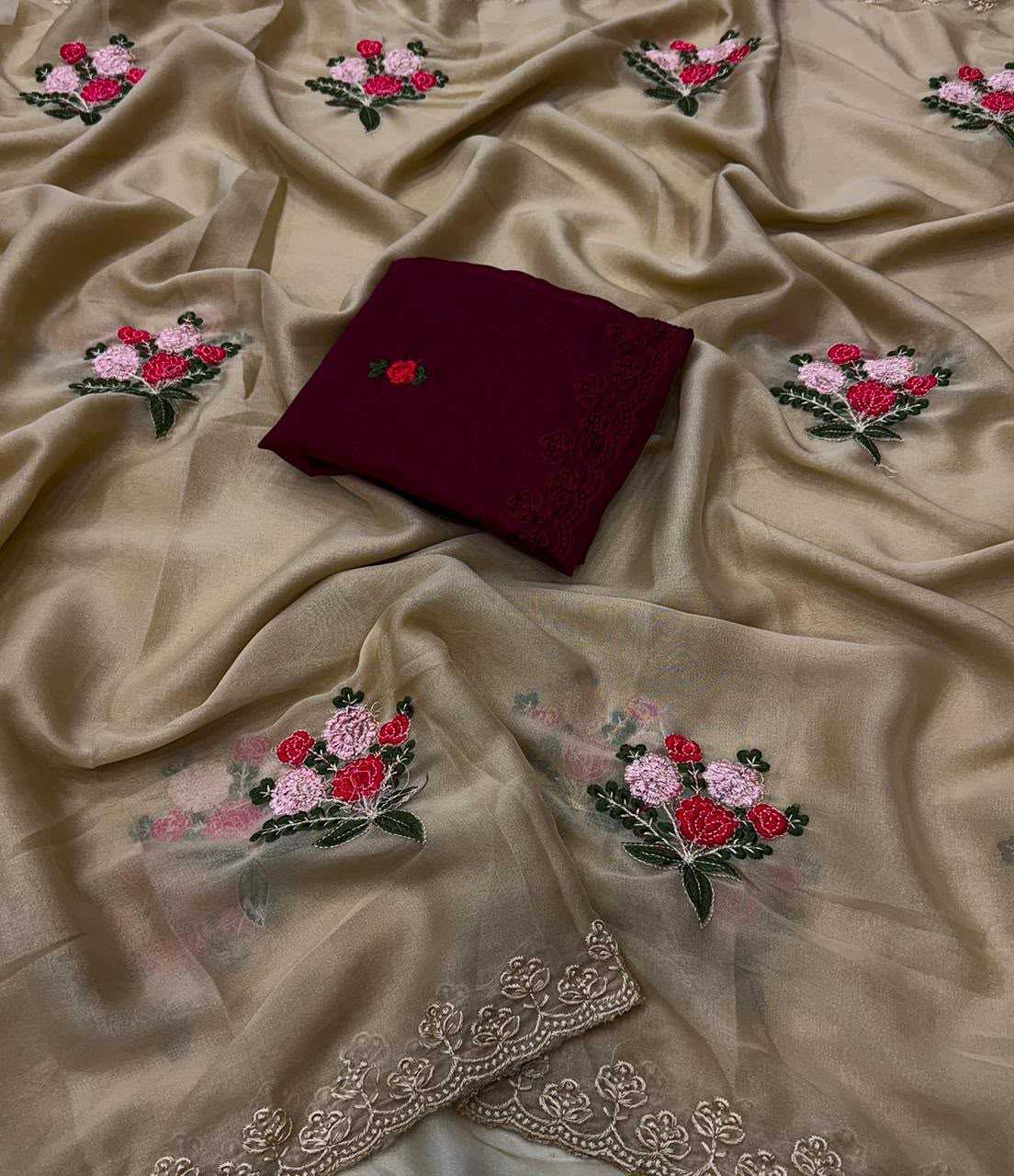 A draped beige sheer fabric with embroidered floral motifs in pink, red, and green, featuring a folded deep maroon fabric piece placed on top.