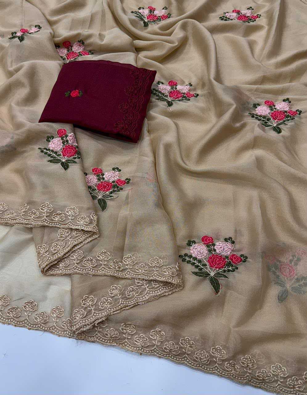 Beige embroidered fabric with floral motifs in pink, red, and green, featuring a matching maroon folded piece with embroidered details.