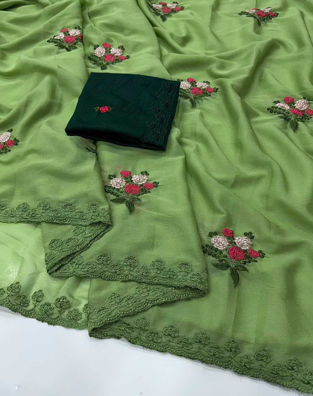 A light green embroidered fabric with matching lace borders and a folded dark green fabric piece placed on top, featuring small floral embroidery in pink, white, and green.