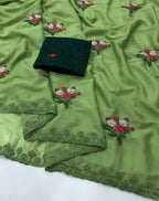 A light green embroidered fabric with matching lace borders and a folded dark green fabric piece placed on top, featuring small floral embroidery in pink, white, and green.
