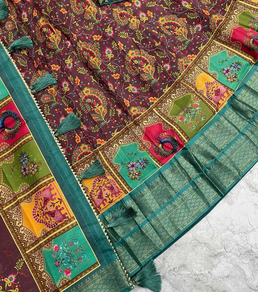 A close-up of a traditional Indian saree fabric featuring a dark purple body with intricate multicolor floral and paisley patterns, a wide border with colorful embroidered panels, and a green pleated pallu with tassels.