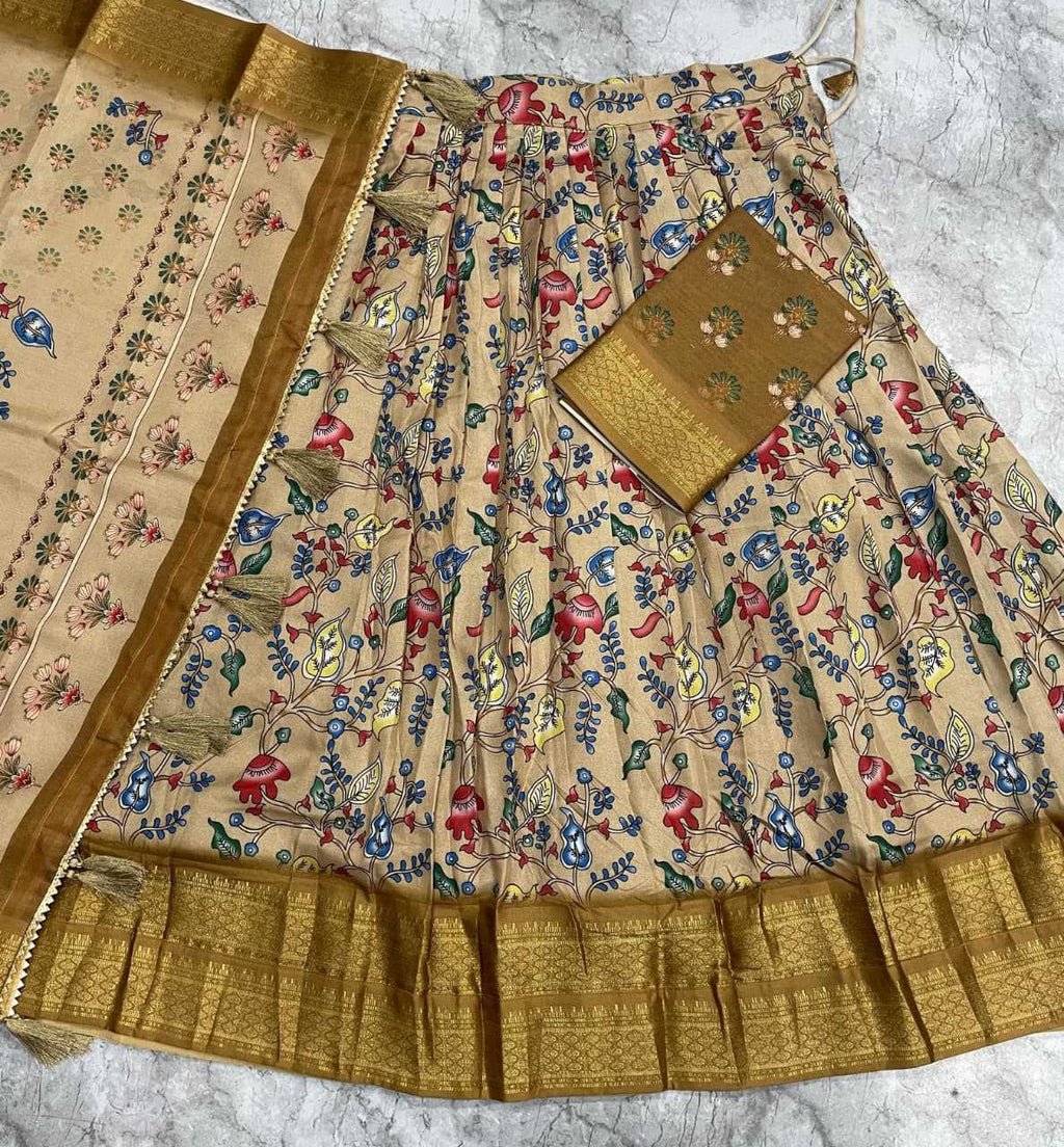 A beige flared skirt or lehenga with dense multicolor floral and bird motifs, finished with a wide metallic gold border, shown laid flat with a matching gold fabric piece on a light stone surface.