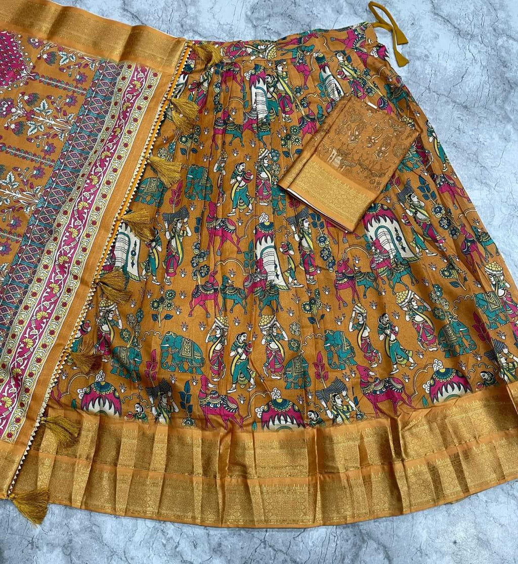 A mustard yellow printed cotton skirt with a wide border and matching fabric pieces laid out on a gray marble surface. The skirt features colorful traditional folk art illustrations and a metallic gold border.