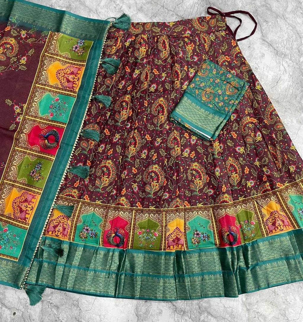 A traditional Indian skirt set with a deep purple body featuring intricate multicolor floral and paisley patterns, a wide green border with colorful motifs, and a matching green embroidered blouse piece, laid flat on a light gray textured surface.