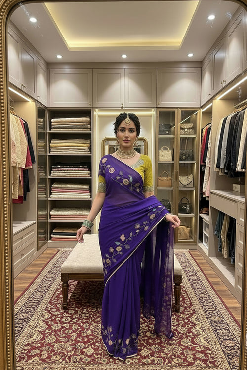A woman takes a mirror selfie in a luxurious walk-in closet, wearing a purple silk saree with gold floral embroidery and a yellow-green blouse.