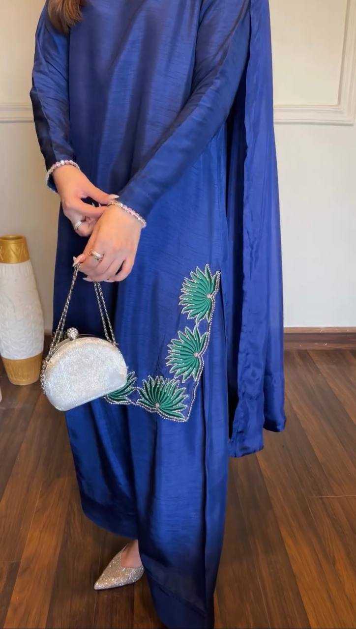 Person wearing a blue dress with green embroidery, holding a white clutch with floral design.