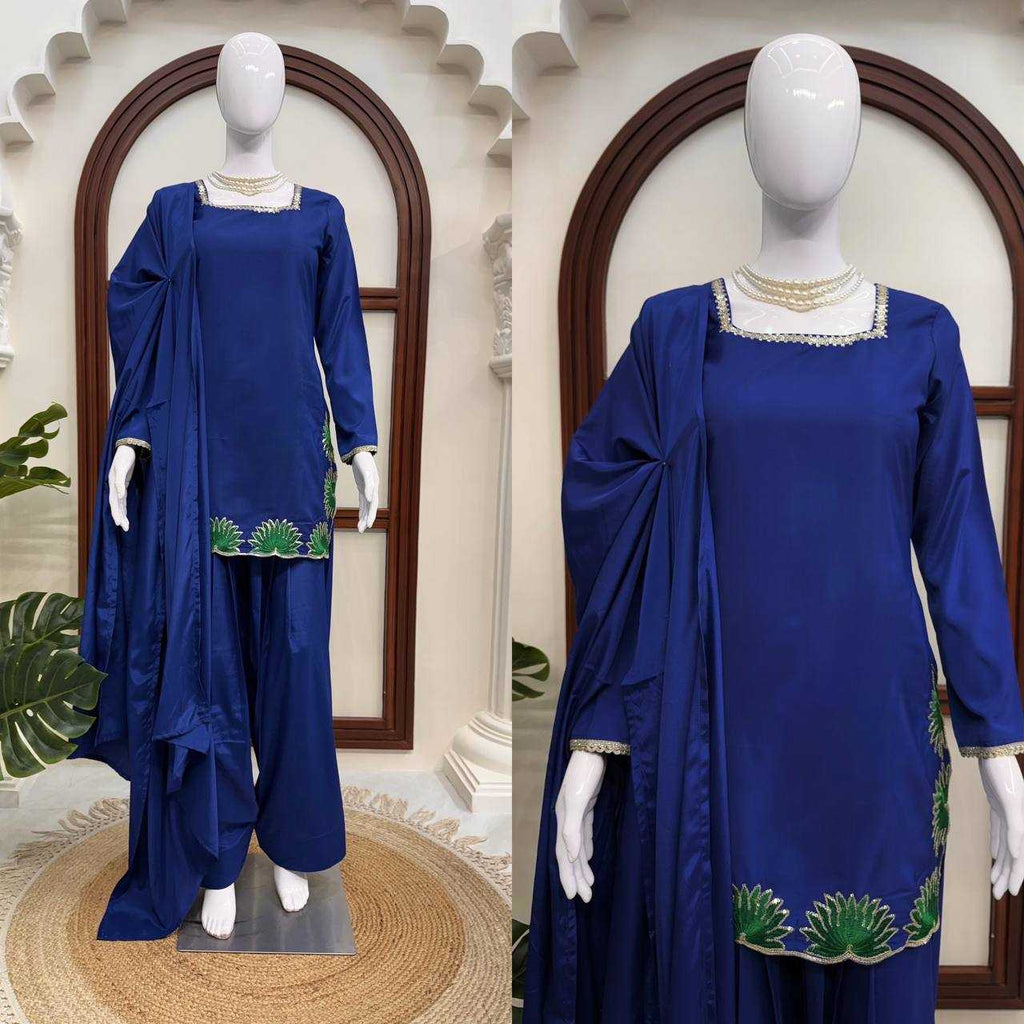 Blue traditional outfit with green embroidery on a mannequin against a decorative wall.