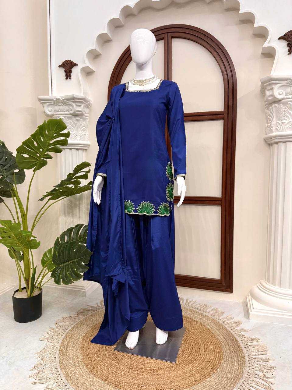 Mannequin wearing a blue traditional outfit with green embroidery in a decorative setting.