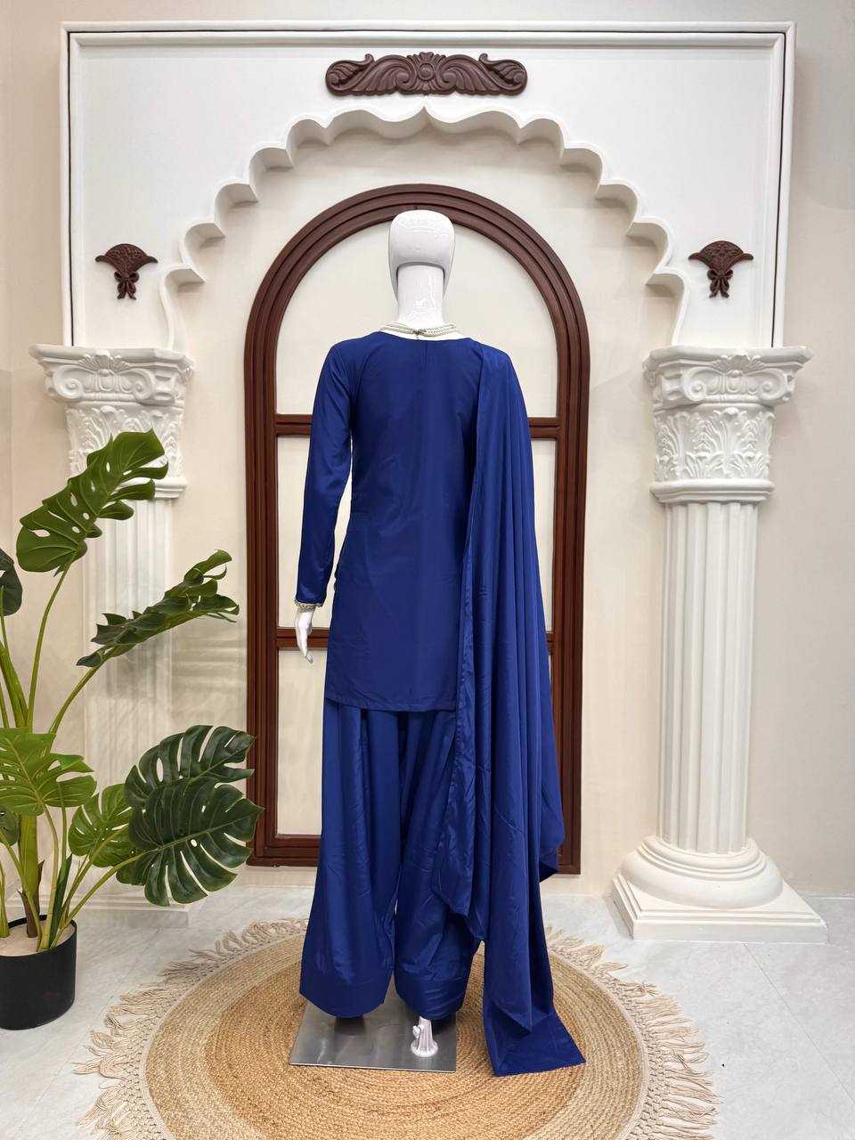 Mannequin wearing a blue traditional outfit in a decorative setting with columns and a plant.