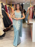Woman in a light blue saree with white embroidery standing in a clothing store.