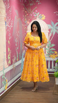 Woman in a yellow floral dress standing in front of a decorative wall with pink and white patterns.