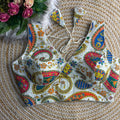 Colorful paisley-patterned bikini set on a textured surface with flowers.