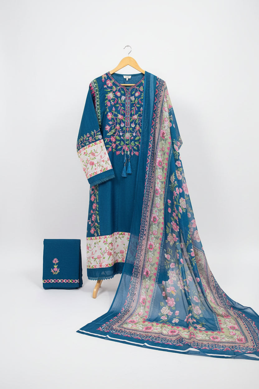 A blue embroidered women's salwar kameez suit set with a floral printed dupatta and matching pants, held up on a hanger by a person in a shop setting. The set features pink, green, and white floral embroidery and prints on a blue base.