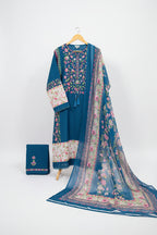 A blue embroidered women's salwar kameez suit set with a floral printed dupatta and matching pants, held up on a hanger by a person in a shop setting. The set features pink, green, and white floral embroidery and prints on a blue base.